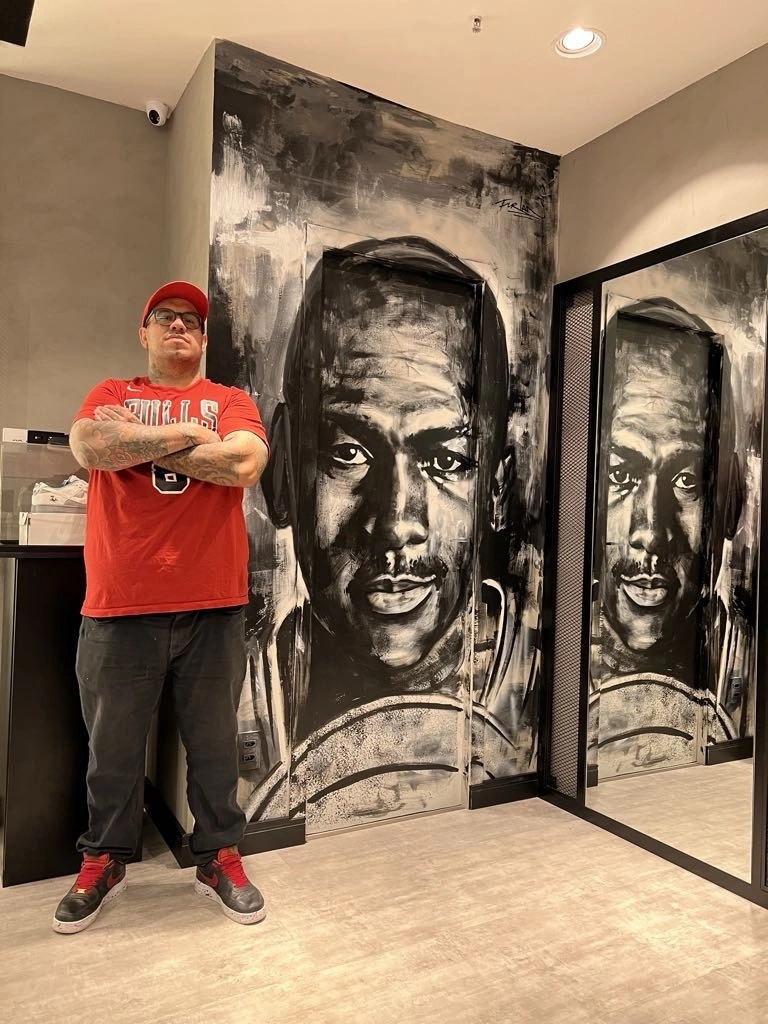 Rafael Furlan junto a mural de retrato em preto e branco em ambiente interior